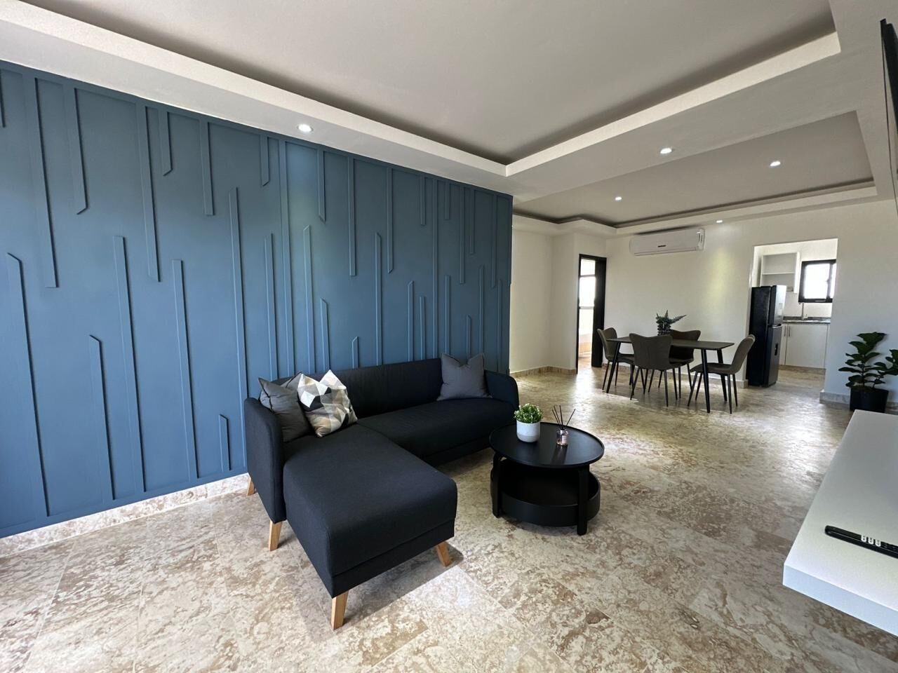 Een moderne woonkamer met een hoekbank, een salontafel en een eethoek op de achtergrond.