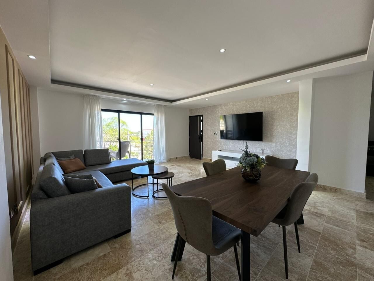 A modern living room with a sofa, dining table, chairs, a TV, and a balcony.