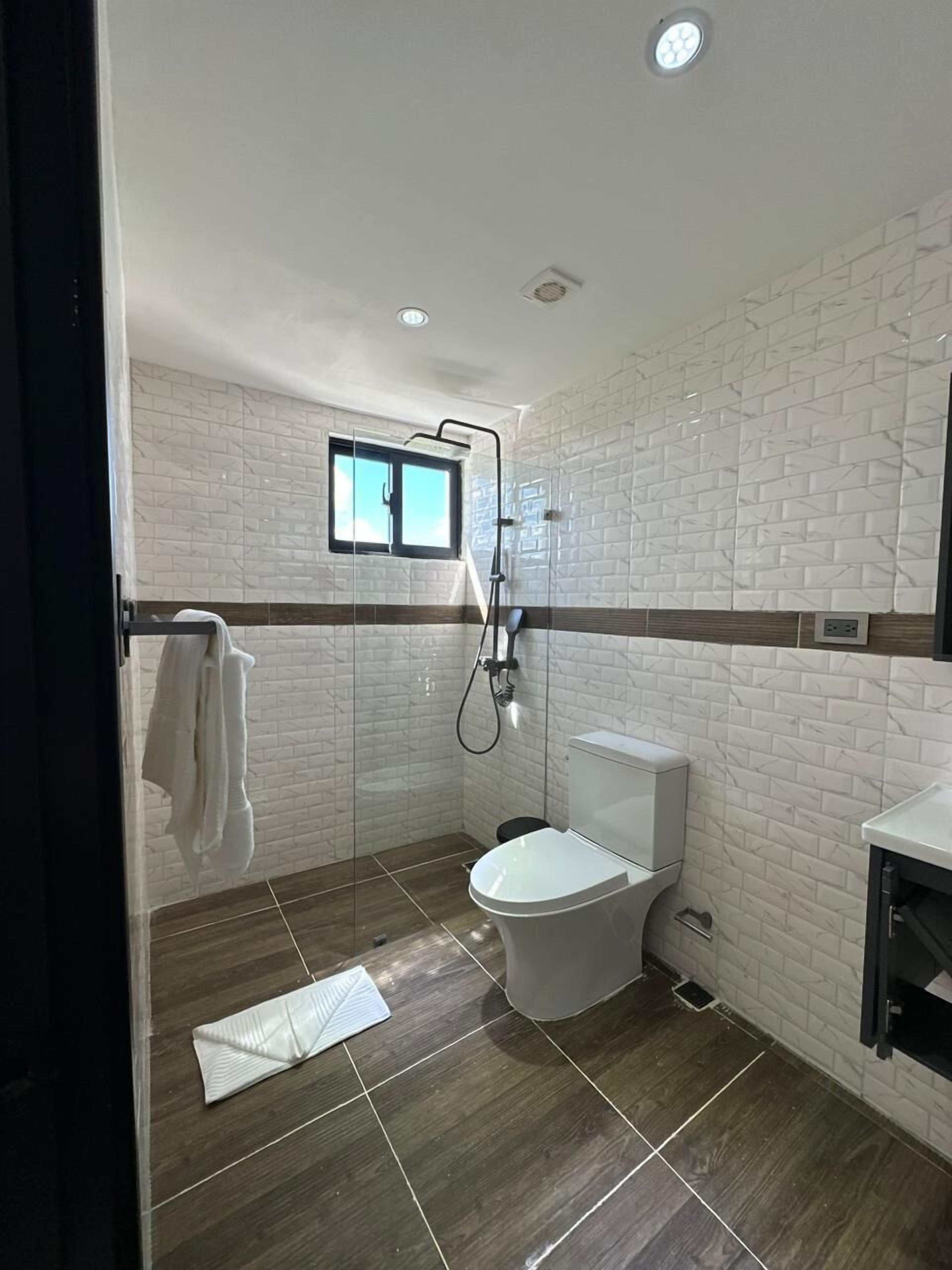 Un baño moderno con azulejos blancos tipo metro, inodoro, ducha y ventana.
