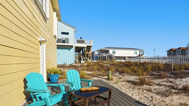 A wooden deck with turquoise Adirondack chairs and a small table, overlooking a sandy beach and a white picket fence. - Sound-View Beach Retreat w/ Multiple Decks, Kayaks & Bikes  Island Vibes (Navarre)