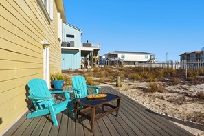 A wooden deck with turquoise Adirondack chairs and a small table, overlooking a sandy beach and a white picket fence. - Sound-View Beach Retreat w/ Multiple Decks, Kayaks & Bikes  Island Vibes (Navarre)