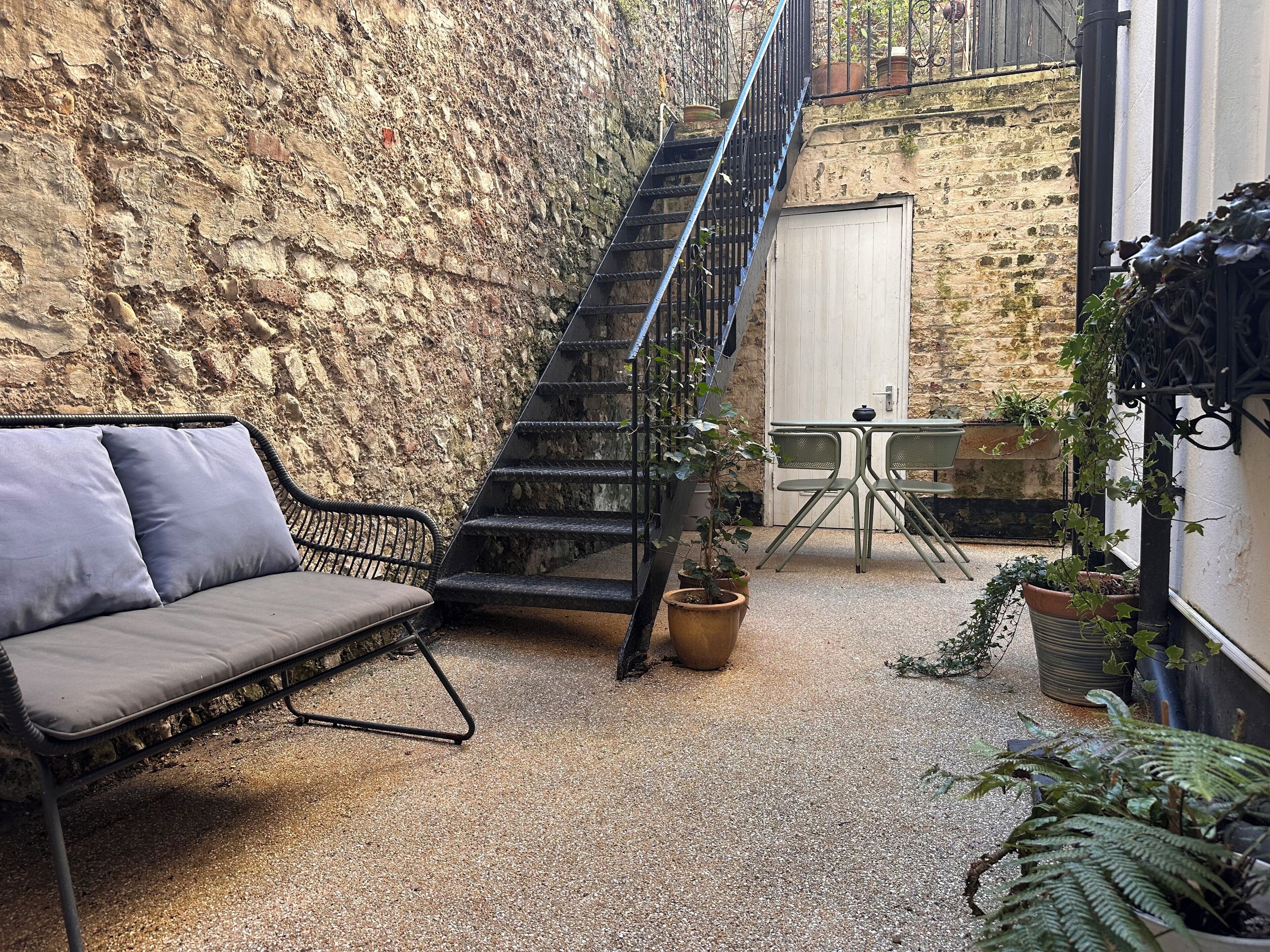 A cozy outdoor seating area with a cushioned bench, a metal staircase, and potted plants.