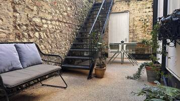A cozy outdoor seating area with a cushioned bench, a metal staircase, and potted plants.