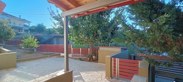 A covered outdoor area with a stone floor, wooden benches, and a metal gate.