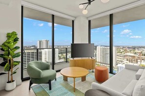 A modern living room with a large window, a flat-screen TV, and a view of the cityscape. - Luxury Downtown Miami Condo | Pool+HotTub+Gym (Miami)