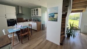 A modern kitchen with white cabinets, a dining area with a table and chairs, and a staircase leading to an upper level. - Crozon-Morgat: Renovated family home for 6-8 people 5 minutes from the beach (Crozon)