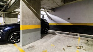 A parking garage with concrete pillars, yellow lines, and a car parked in the distance. - Ape Novo ao lado do Bourbon e Allianz. (São Paulo)