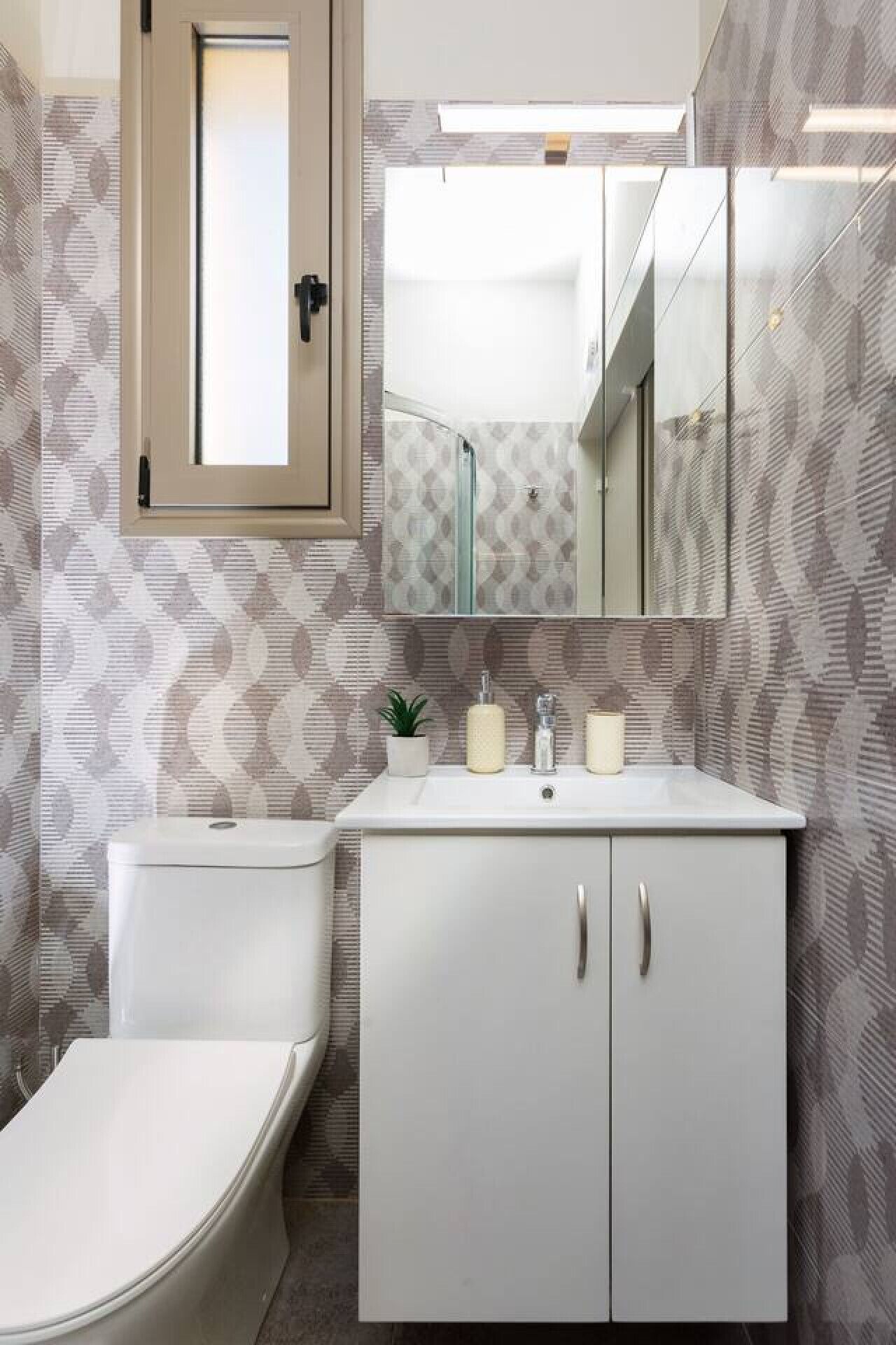Ein Badezimmer mit Toilette, Waschbecken mit Spiegel darüber und strukturierten Tapeten.