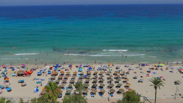 Une plage avec des parasols et des gens, un ciel dégagé et l’océan.