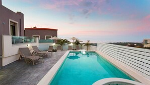 Une piscine sur le toit, dotée de chaises longues et de parasols, offrant une vue dégagée sur le paysage urbain et un ciel au coucher du soleil.