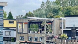 A floating house with a deck, potted plants, and bicycles. - Nova Houseboat Deluxe + free bikes (Amsterdam)