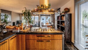 A modern kitchen with wooden cabinets, a central island, and a large window with blinds. - Nova Houseboat Deluxe + free bikes (Amsterdam)