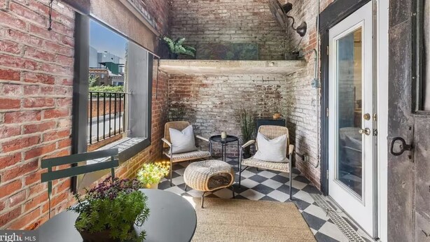 Ein gemütlicher Balkon mit Backsteinwänden, zwei Korbstühlen, einem kleinen runden Tisch und einem Blumentopf.