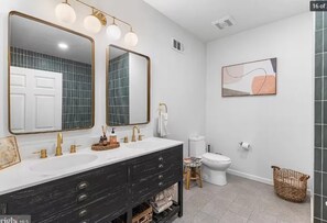 Een moderne badkamer met twee wasbakken, een toilet en een douchegedeelte.