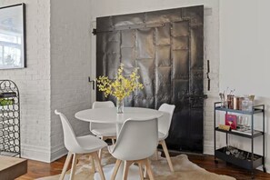Een eetgedeelte met een ronde tafel, witte stoelen, een vaas met gele bloemen en een zwarte metalen deur.