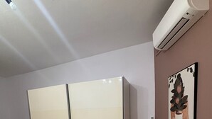 Un dormitorio con cama, armario, estante pequeño y aire acondicionado.