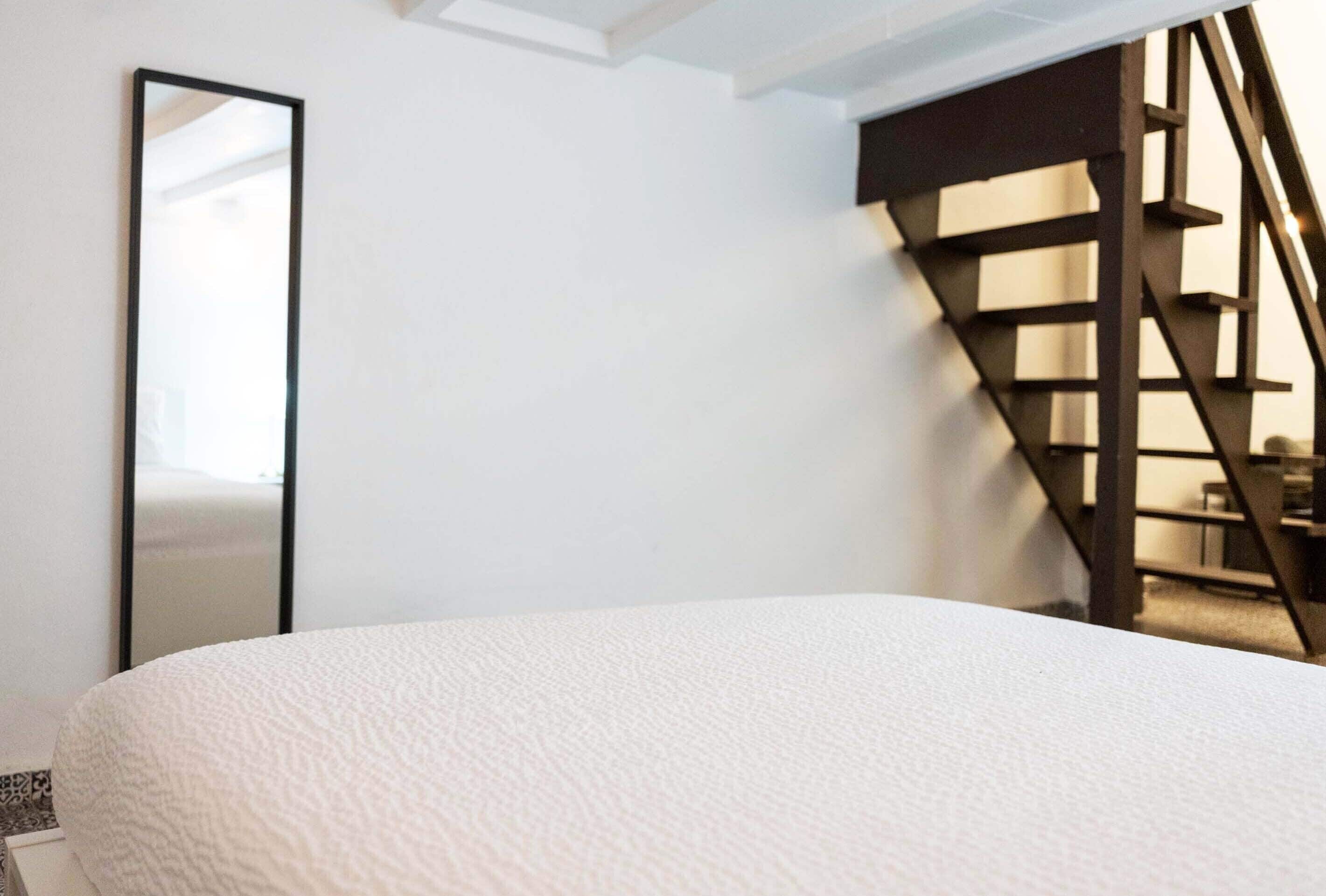 Une chambre à coucher avec un lit, un grand miroir et un escalier en bois.