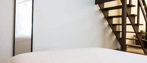 Une chambre à coucher avec un lit, un grand miroir et un escalier en bois.