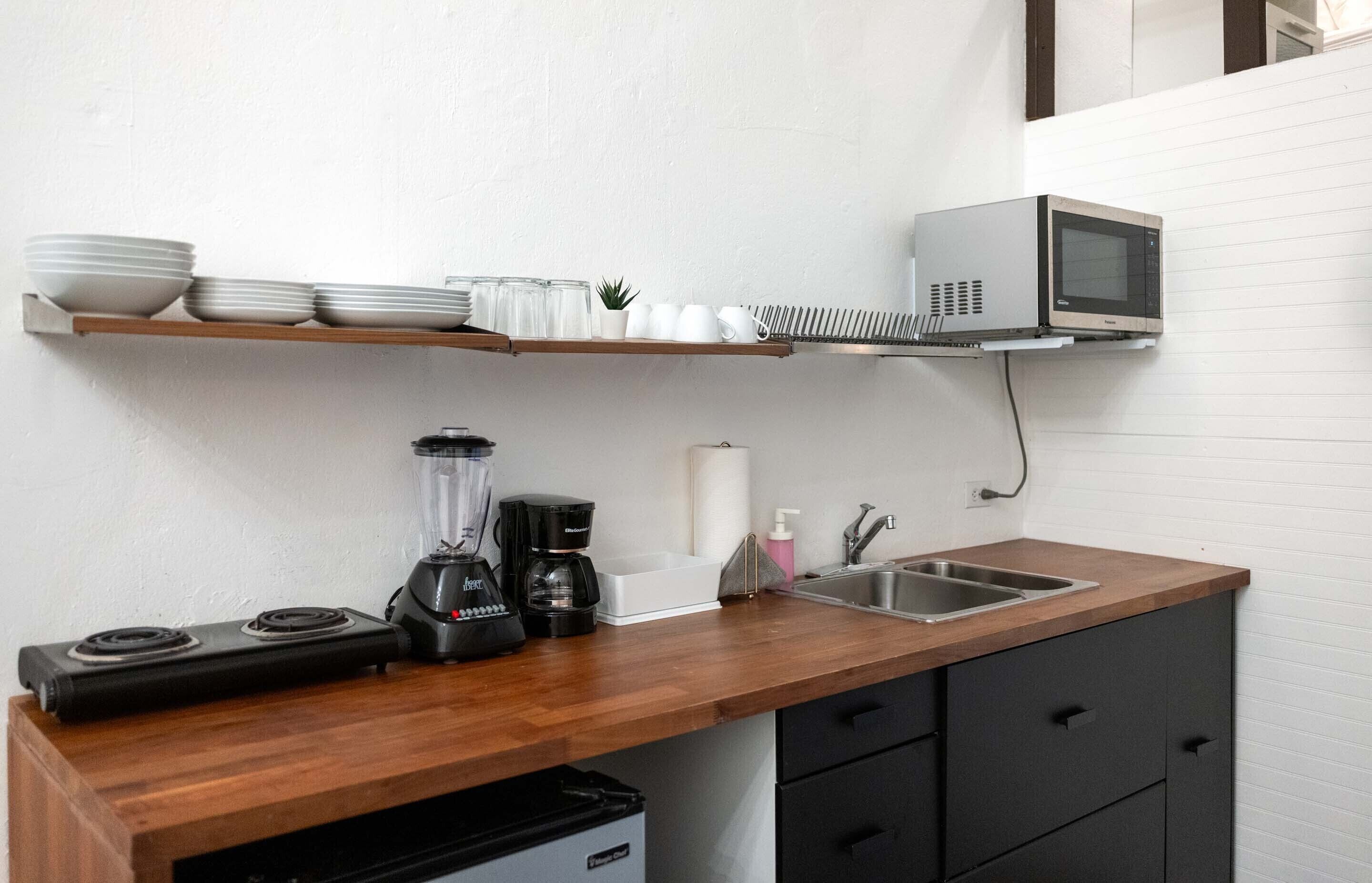 Ett kök med mikrovågsugn, mixer, kaffebryggare och diskho.