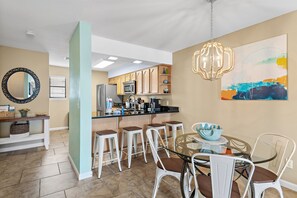 A modern kitchen with a central island, bar stools, and a dining table with chairs. - 🌞🌴Walk to the Beach | Balcony Views | Costa Vista Townhouse #2🌴🌞 (Miramar Beach)