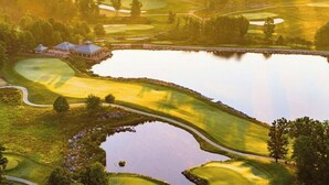 Un campo de golf con un estanque, un club de campo y árboles circundantes.