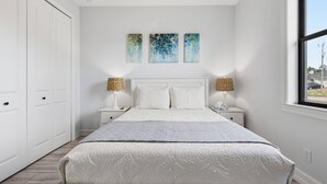 A bedroom with a large bed, white walls, and a window. There are three paintings on the wall above the bed. - 1720 SW 19th PL (Cape Coral)