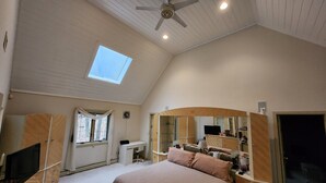 Ein Schlafzimmer mit einem großen Bett, einem Schreibtisch, einem Stuhl, einem Deckenventilator, einem Oberlicht und einem Kleiderschrank.