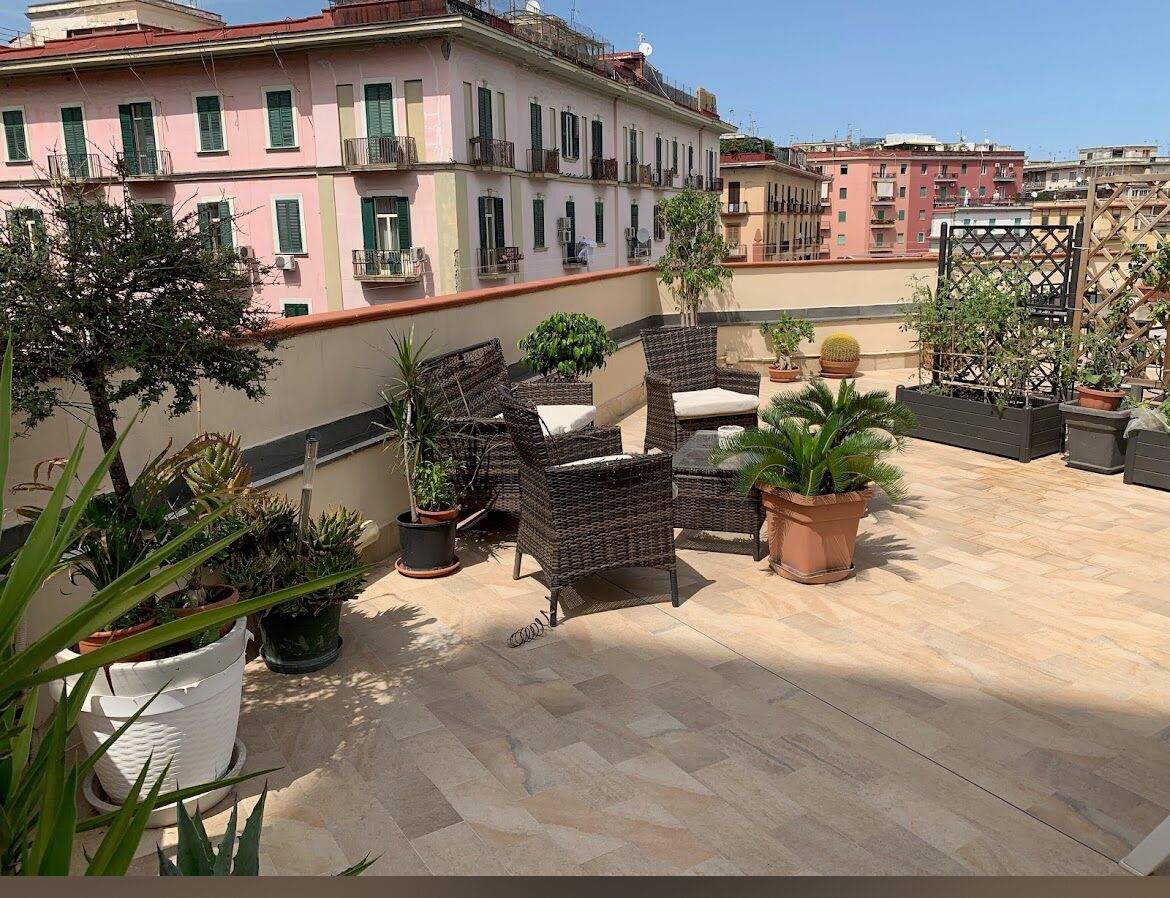 A rooftop terrace with wicker furniture, potted plants, and a view of surrounding buildings.