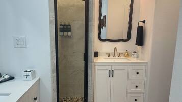 A bathroom with a white vanity, a large mirror, and a shower area.