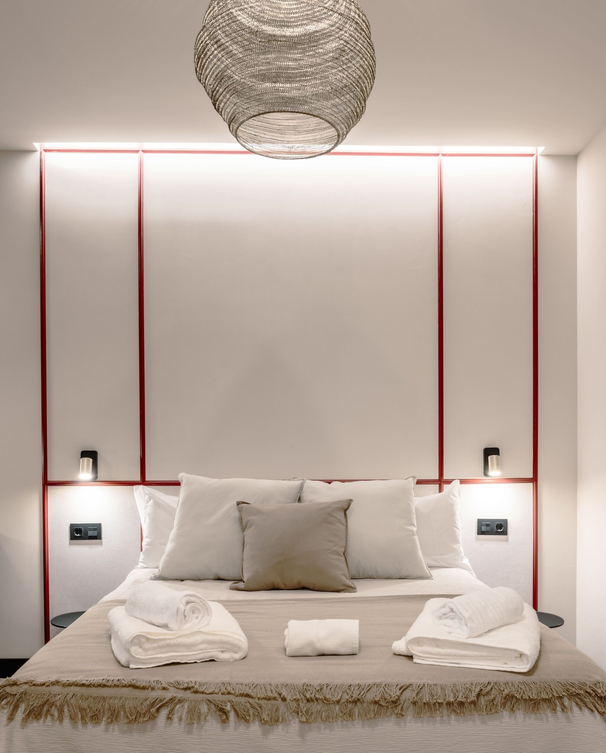 Une chambre d’hôtel moderne équipée d’un lit, de lampes de chevet, d’un luminaire fixé au mur et d’un panneau de commande.