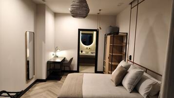 A modern bedroom with a bed, bedside table, lamp, wardrobe, and a mirror reflecting a bathroom.