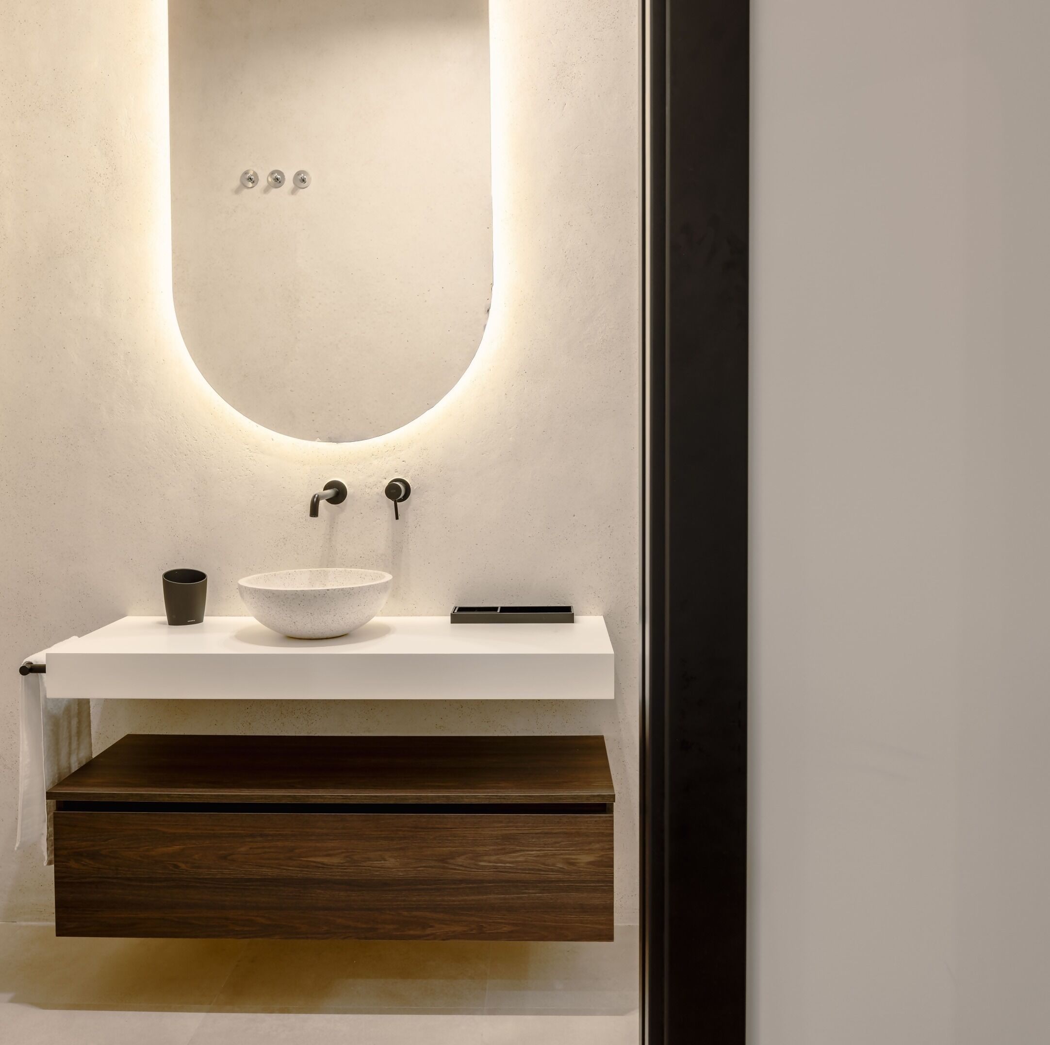 Een moderne badkamer met een witte wastafel, een kom, een beker en een houten lade.