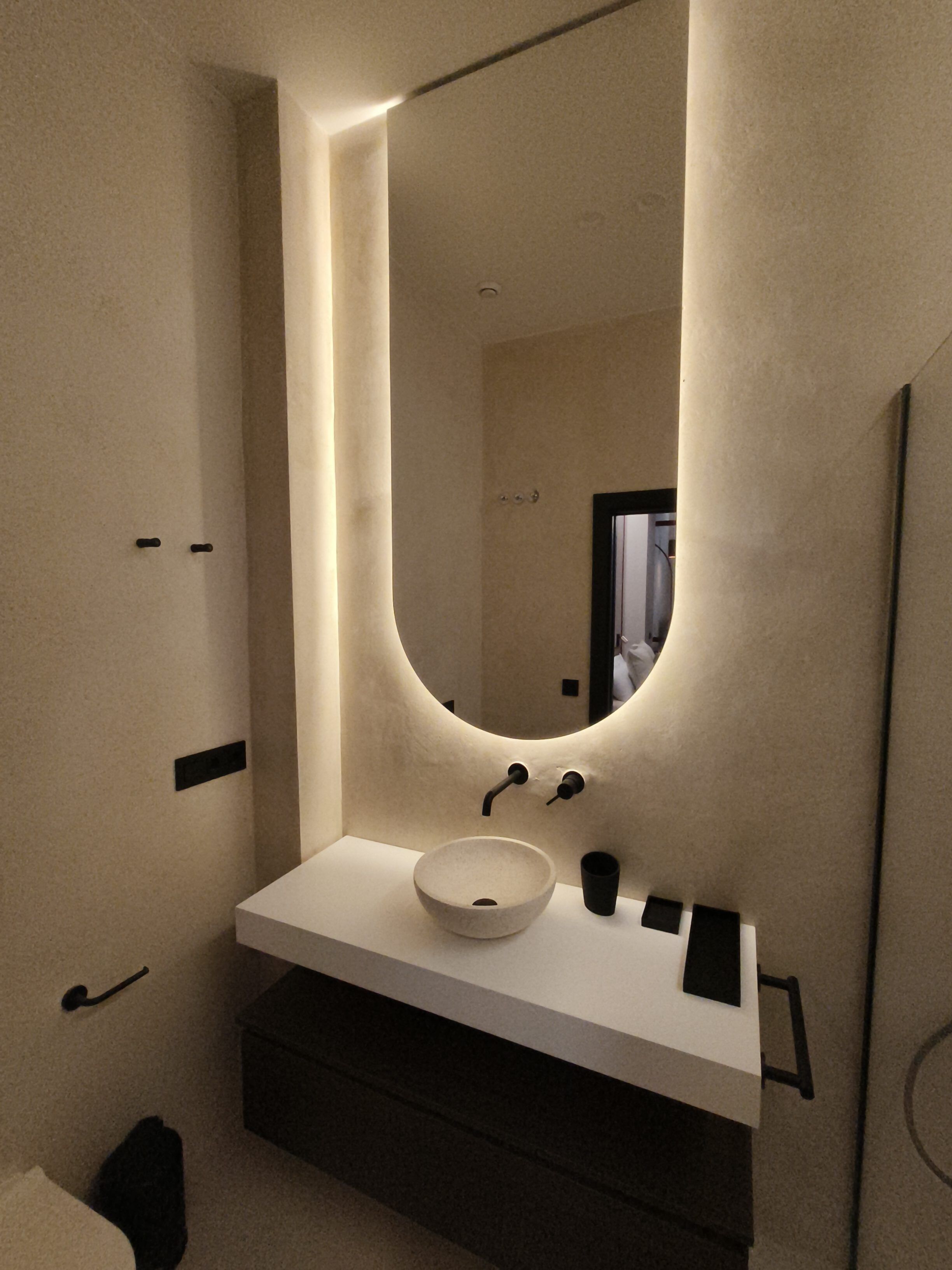 Une salle de bain moderne avec un grand miroir, un lavabo blanc et un plan de toilette noir.