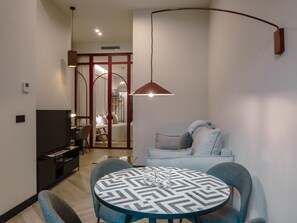 Een moderne woonkamer met een ronde eettafel, twee stoelen, een bank, een televisie en een hangende hanglamp.