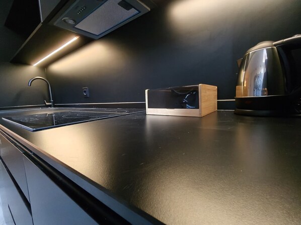 Une cuisine moderne avec un élégant plan de travail noir, une bouilloire en acier inoxydable et une boîte en bois.