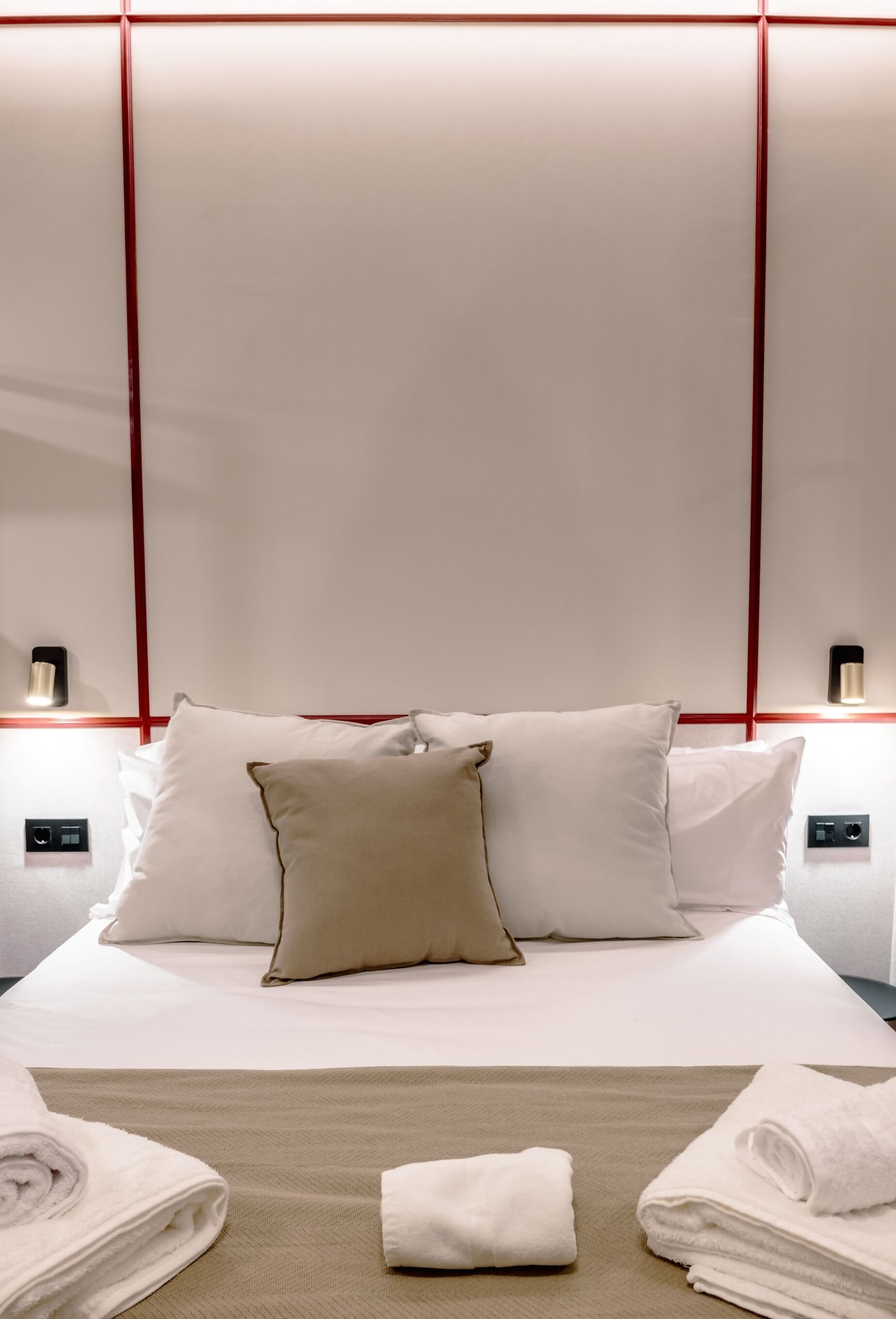 A hotel room with a neatly made bed, two bedside lamps, and a wall-mounted light fixture.