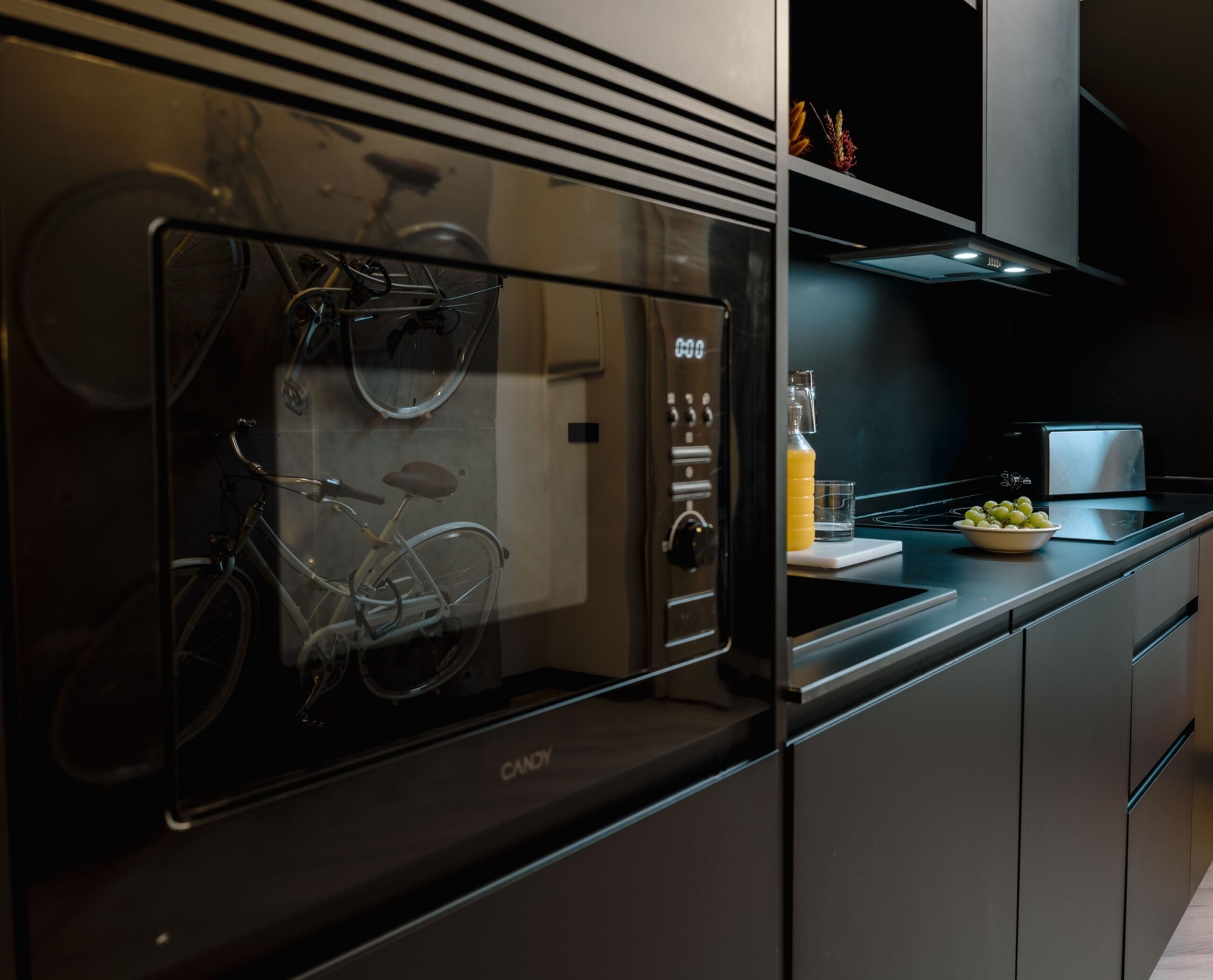 Una cocina moderna con horno empotrado, refrigerador con puerta de vidrio y una bicicleta en su interior.