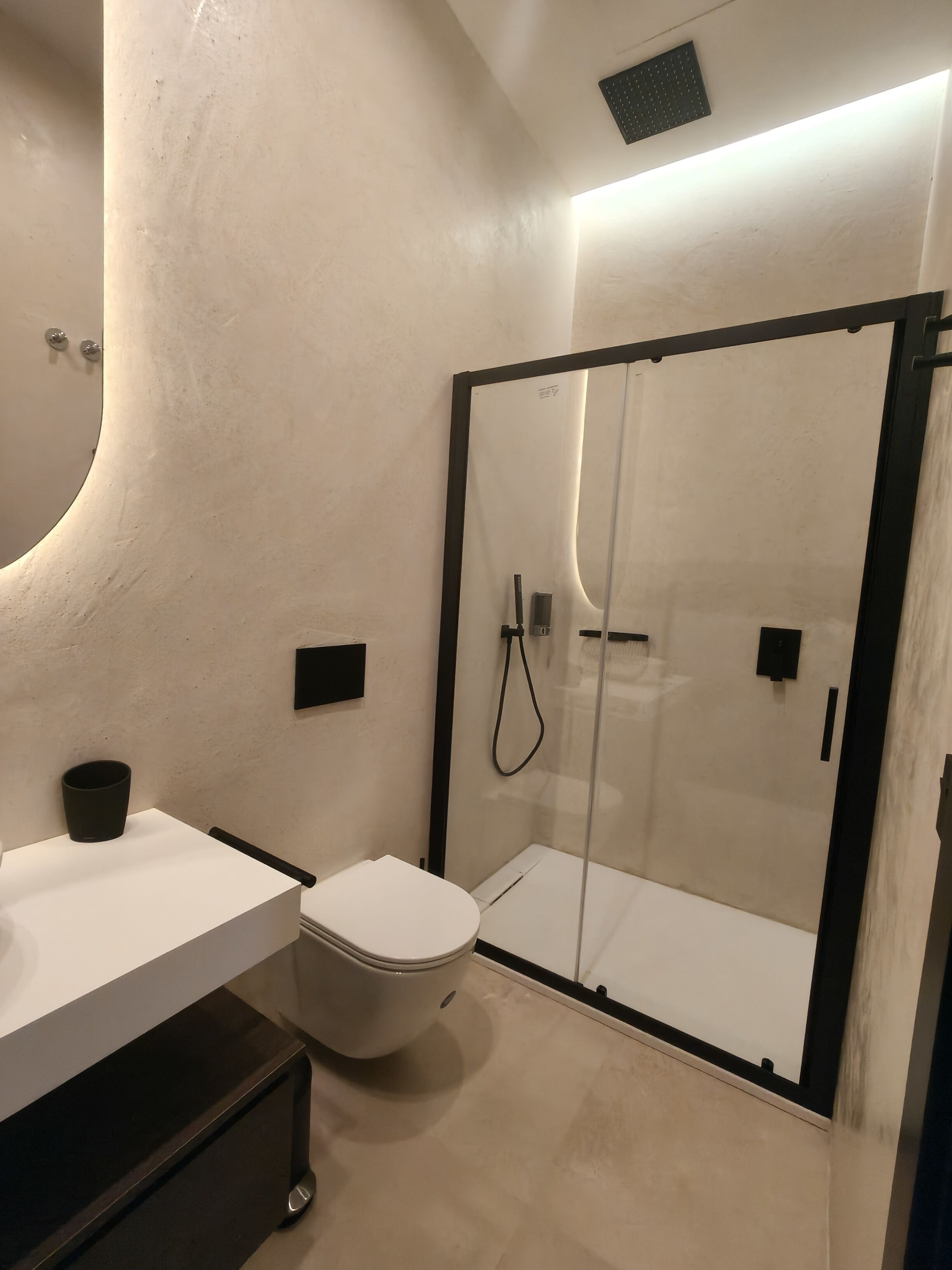 Une salle de bain moderne équipée de toilettes, d’un lavabo et d’une douche séparée par une paroi en verre.