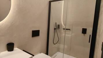 Une salle de bain moderne équipée de toilettes, d’un lavabo et d’une douche séparée par une paroi en verre.