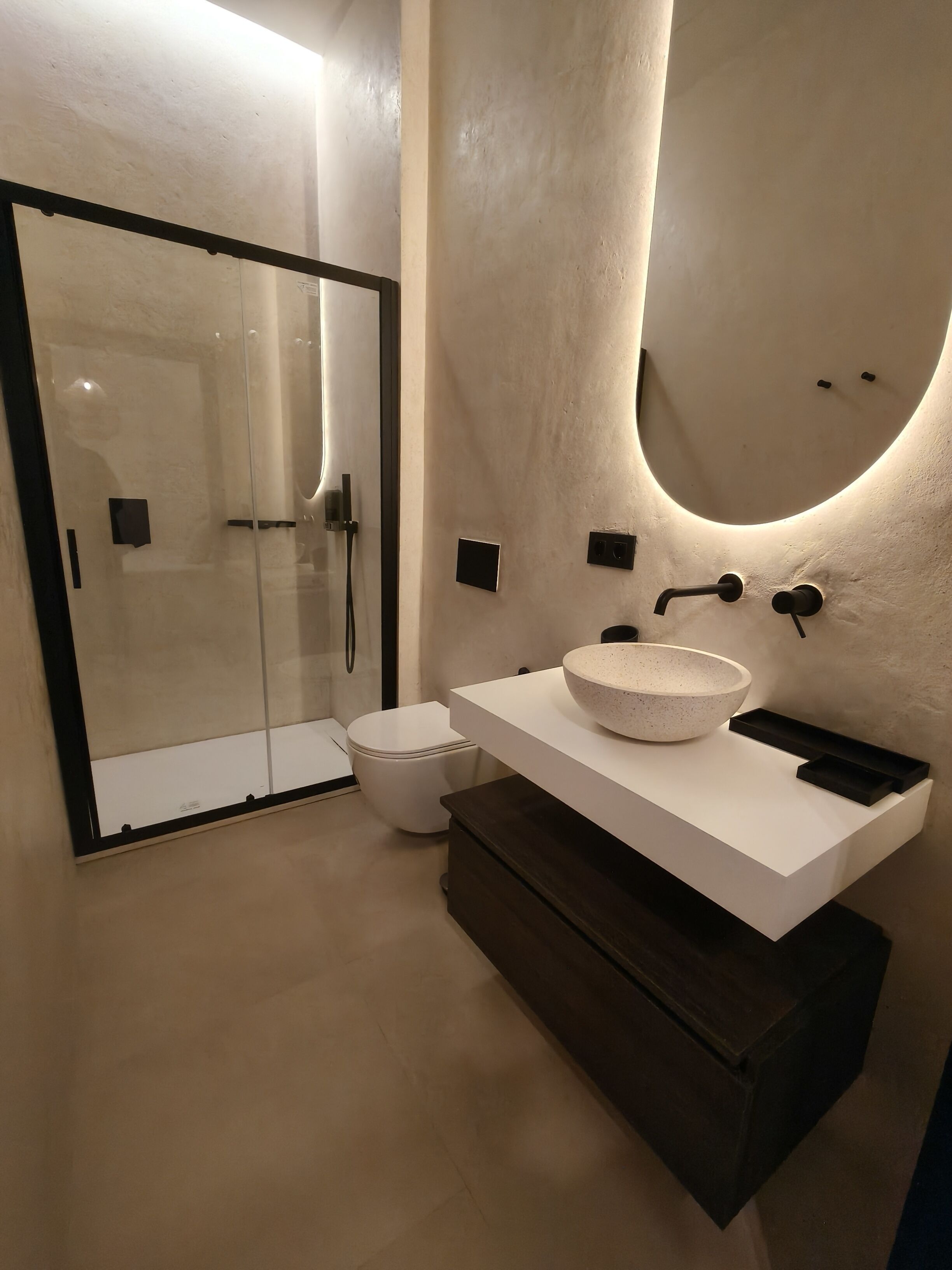 Une salle de bain moderne avec une douche à parois de verre, un lavabo blanc à cuve mouchetée et un meuble en bois foncé.