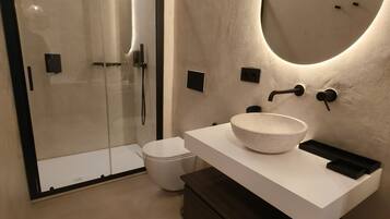Une salle de bain moderne avec une douche à parois de verre, un lavabo blanc à cuve mouchetée et un meuble en bois foncé.