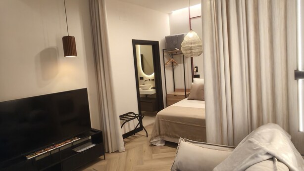 Une chambre d’hôtel moderne équipée d’une télévision à écran plat, d’un canapé, d’une table basse en verre et d’un lit avec une literie blanche.