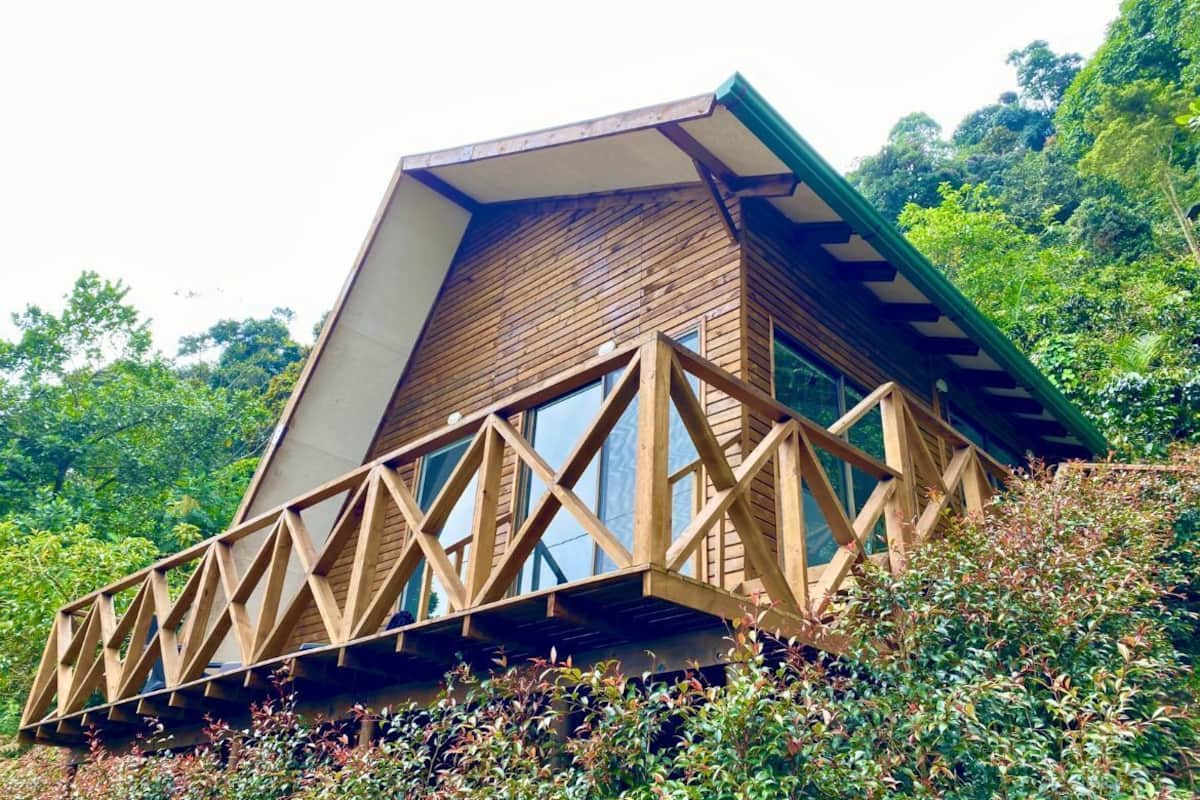 A triangular wooden structure with a balcony, surrounded by lush greenery.