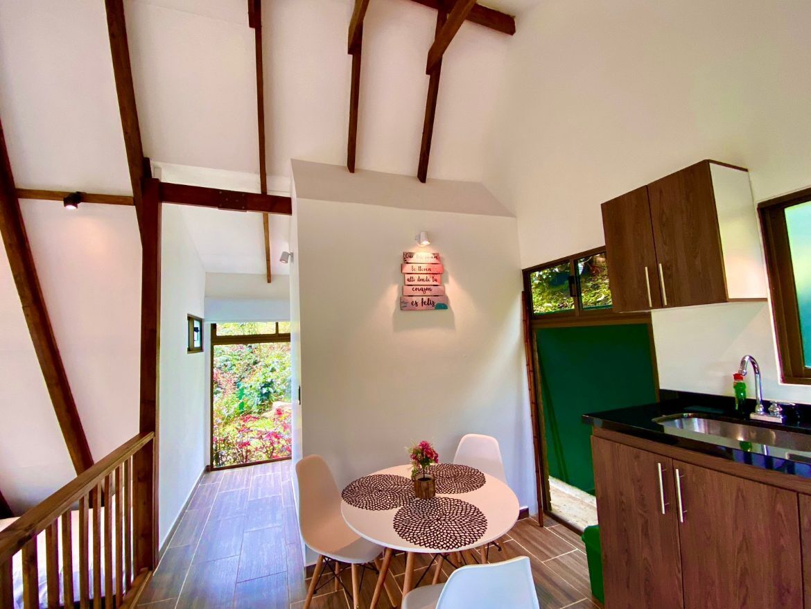 Un coin repas avec une table ronde et des chaises, une cuisine avec des meubles en bois et un escalier avec des poutres apparentes.