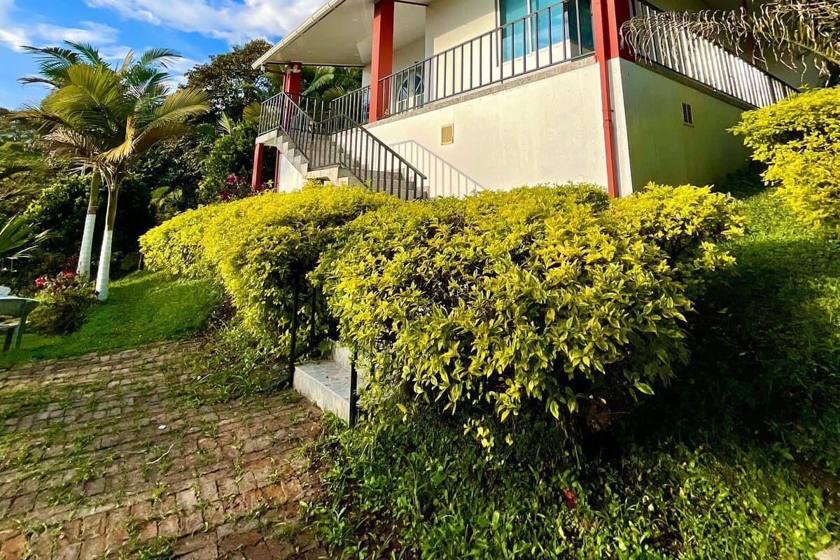 A two-story building with a balcony, surrounded by well-maintained hedges and palm trees.