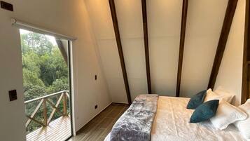 Un dormitorio con una cama grande, un balcón con barandilla de madera y vistas a zonas verdes.