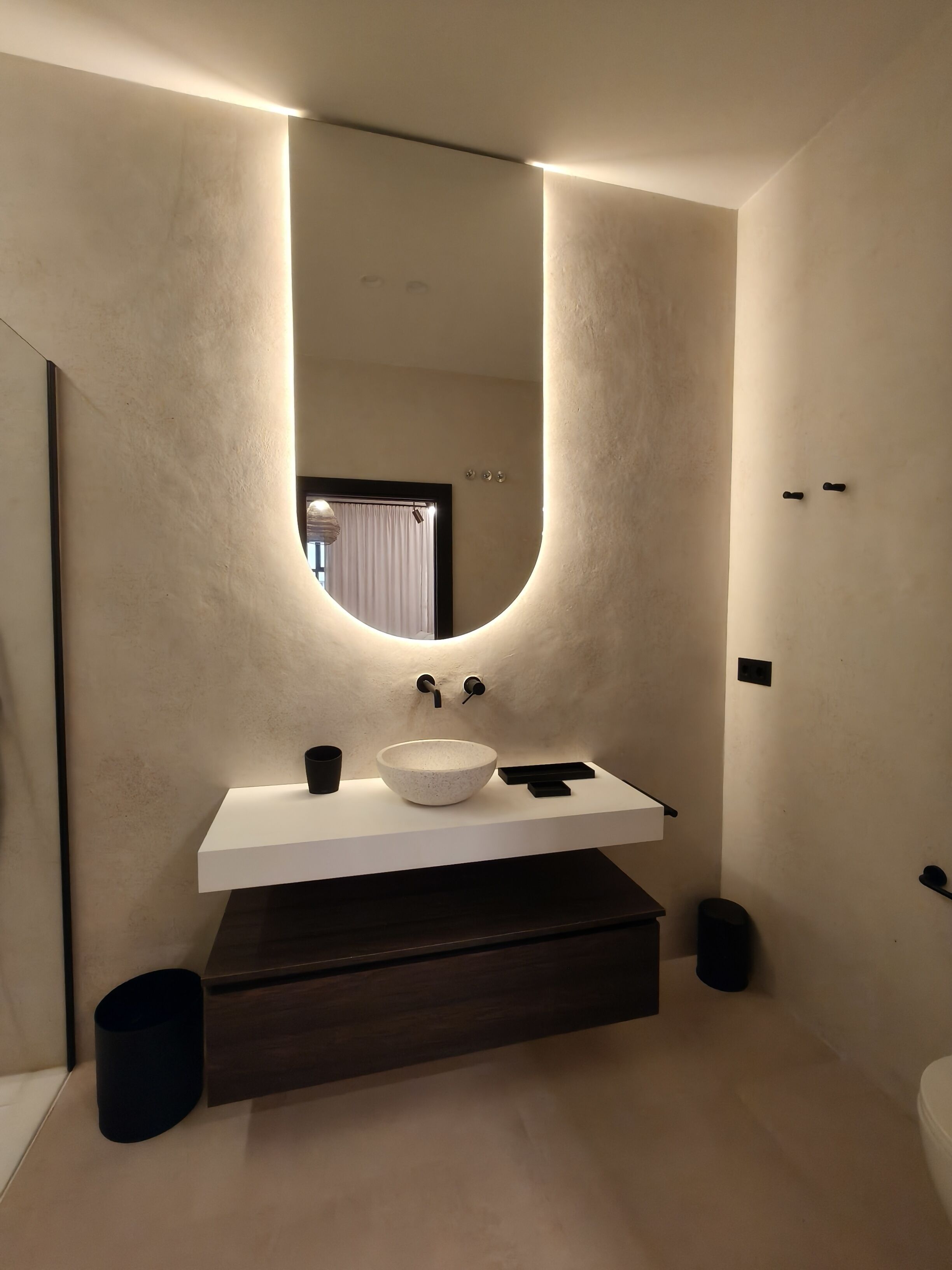 A modern bathroom with a large mirror, a white sink, and a dark wooden vanity.
