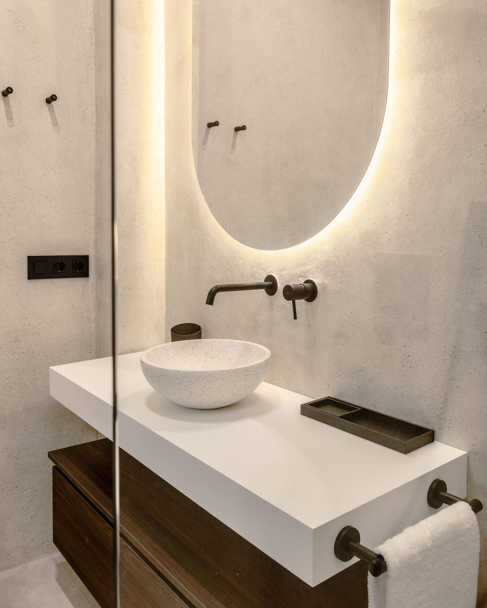 Un bany modern amb un lavabo blanc, un mirall rodó i un armari de fusta.