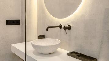 Un bany modern amb un lavabo blanc, un mirall rodó i un armari de fusta.