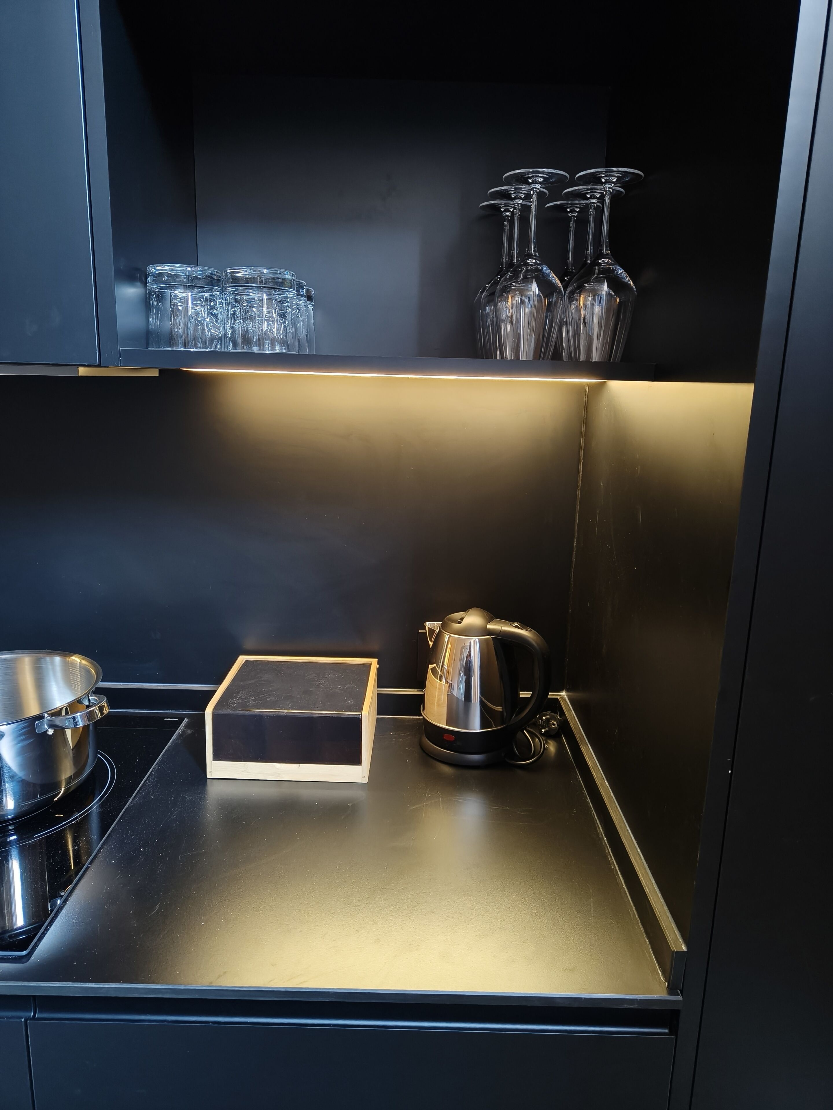 Une cuisine dotée d’un plan de travail en acier inoxydable, d’une bouilloire, d’une casserole et de verres disposés sur des étagères.
